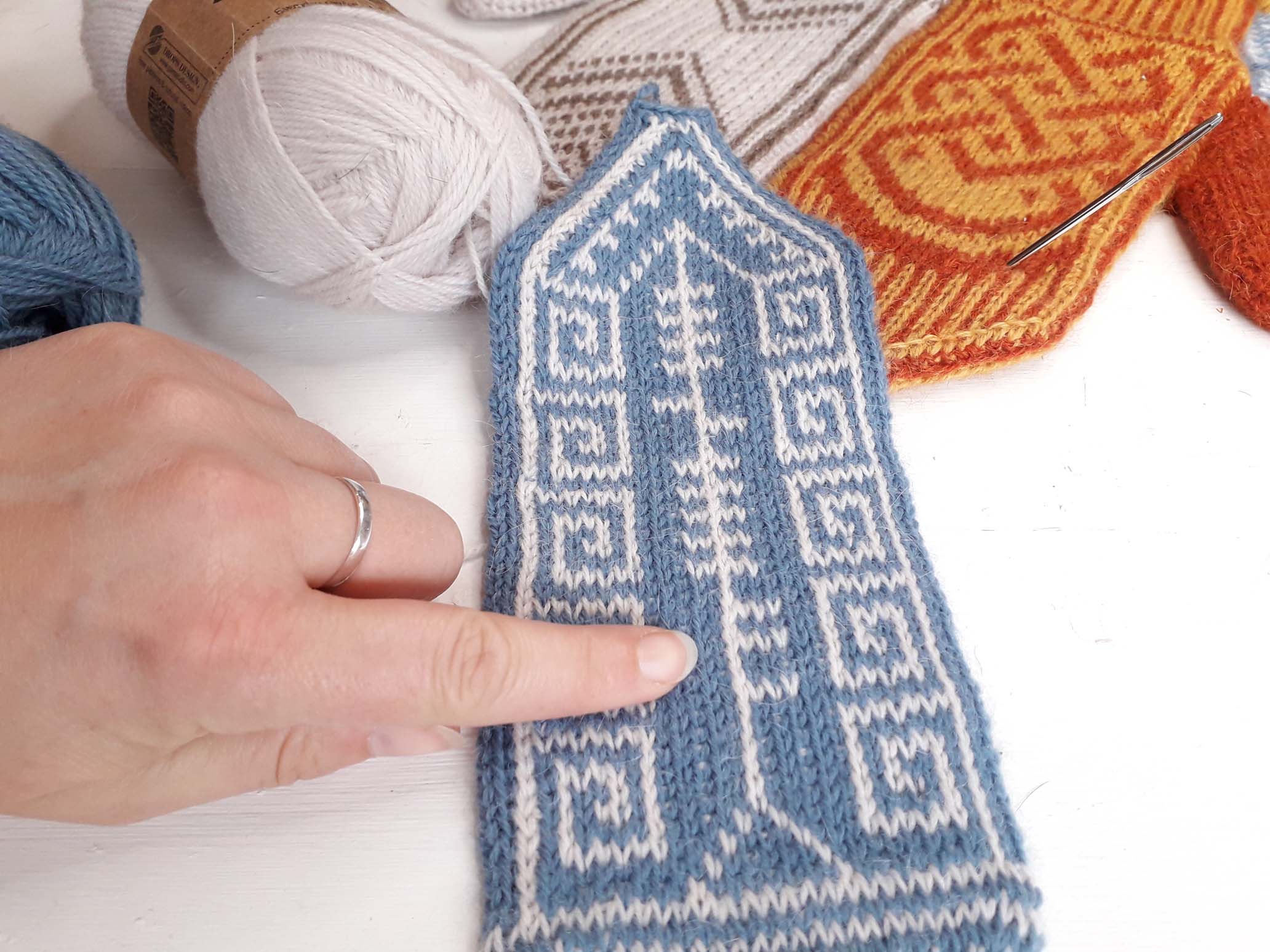 An index finger points at a stitch on a stranded colorwork mitten. 